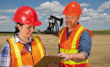 2 petroleum workers discussing a document against a background of horsehead pumps.
